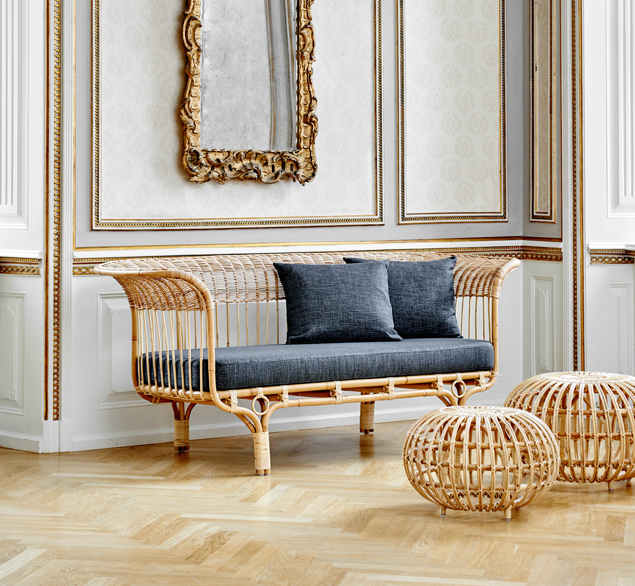 This is a lifestyle image of Belladonna Sofa in polished natural rattan, in a bright Scandinavian interior seen through a white doorway.