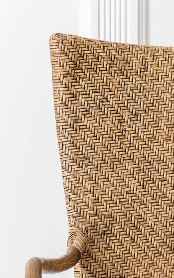 This is a close-up image of Melody Dining Armchair in antique rattan. Detail of the herringbone weave backrest and curved rattan armrest.