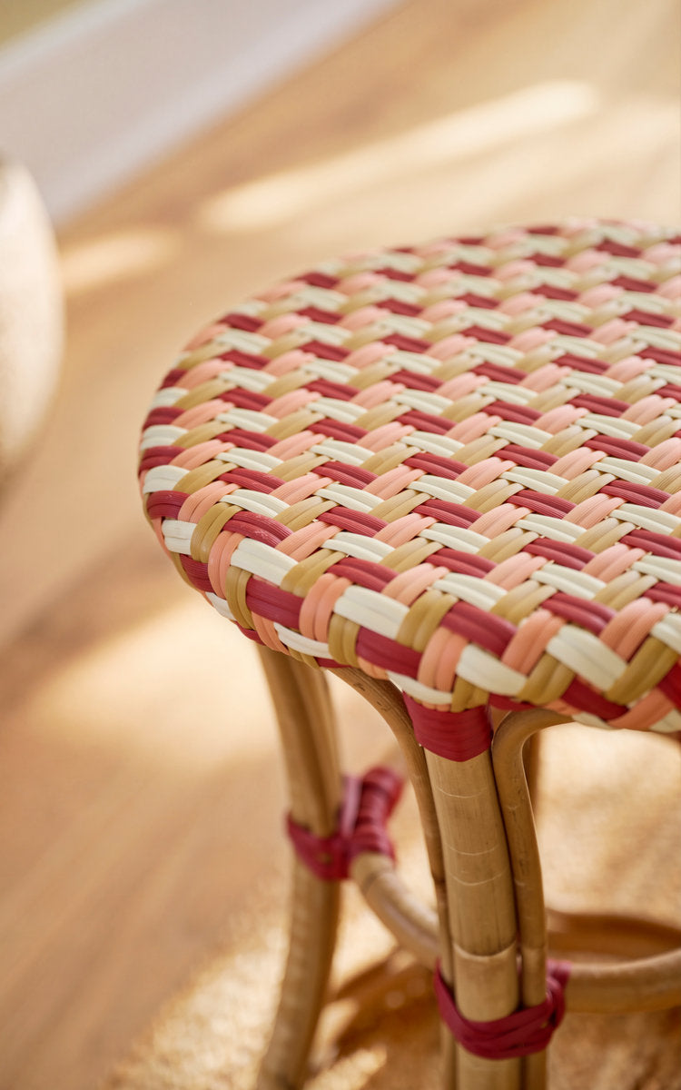 This is a close-up image of Chloe Stool in zigzag weave ivory honey coral burgundy red skin on rattan frame. Zigzag woven seat in warm, sunlit tones.