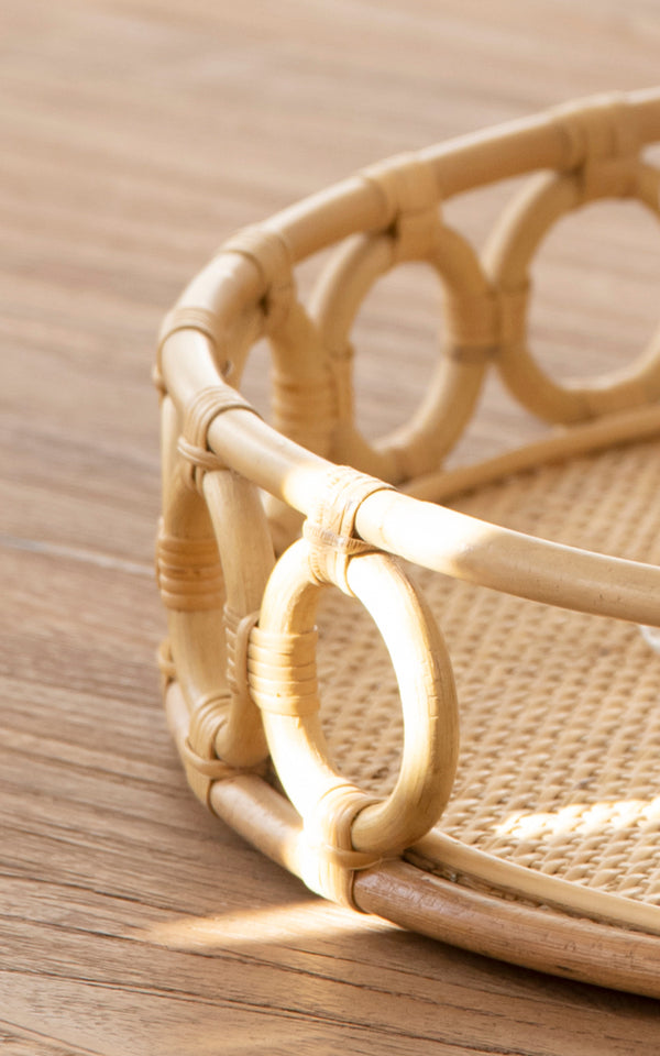 This is a close-up image of Mira Tray in natural rattan. Detail of the circular ring border and woven cane base of the round tray.