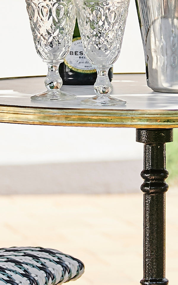 This is a close-up image of Lyon Café Table Versalite Marble Ø70 cm in cast iron. Marble top edge with brass rim and ornate iron pedestal.