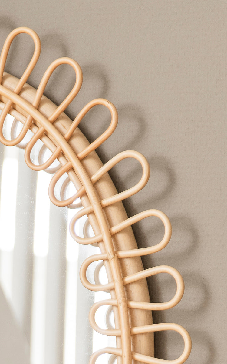 This is a close-up image of Luella Mirror in polished natural rattan. The decorative looped rattan frame casts elegant shadows on the wall.
