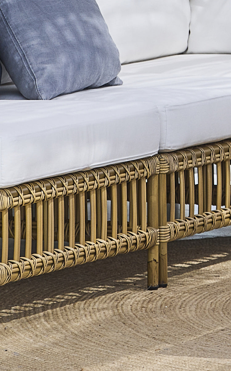 This is a close-up image of Maggie Sofa Center Module in antique aluminium artfibre. Base frame with cross-weave detail and jute rug beneath.