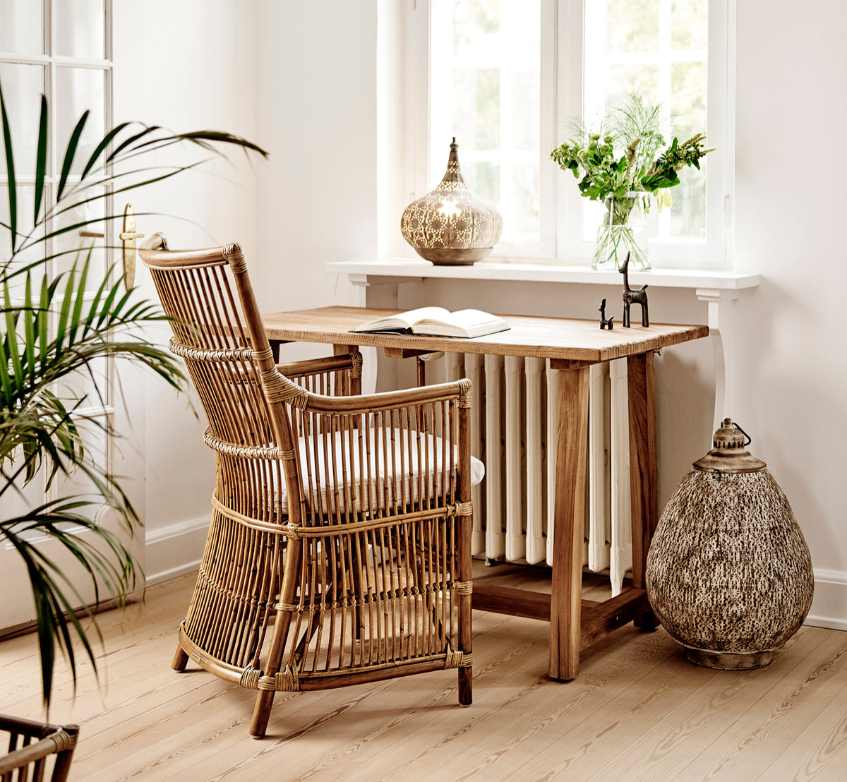 This is a lifestyle image of Davinci Dining Chair in antique rattan, in a bright interior with white panelled walls and herringbone parquet.