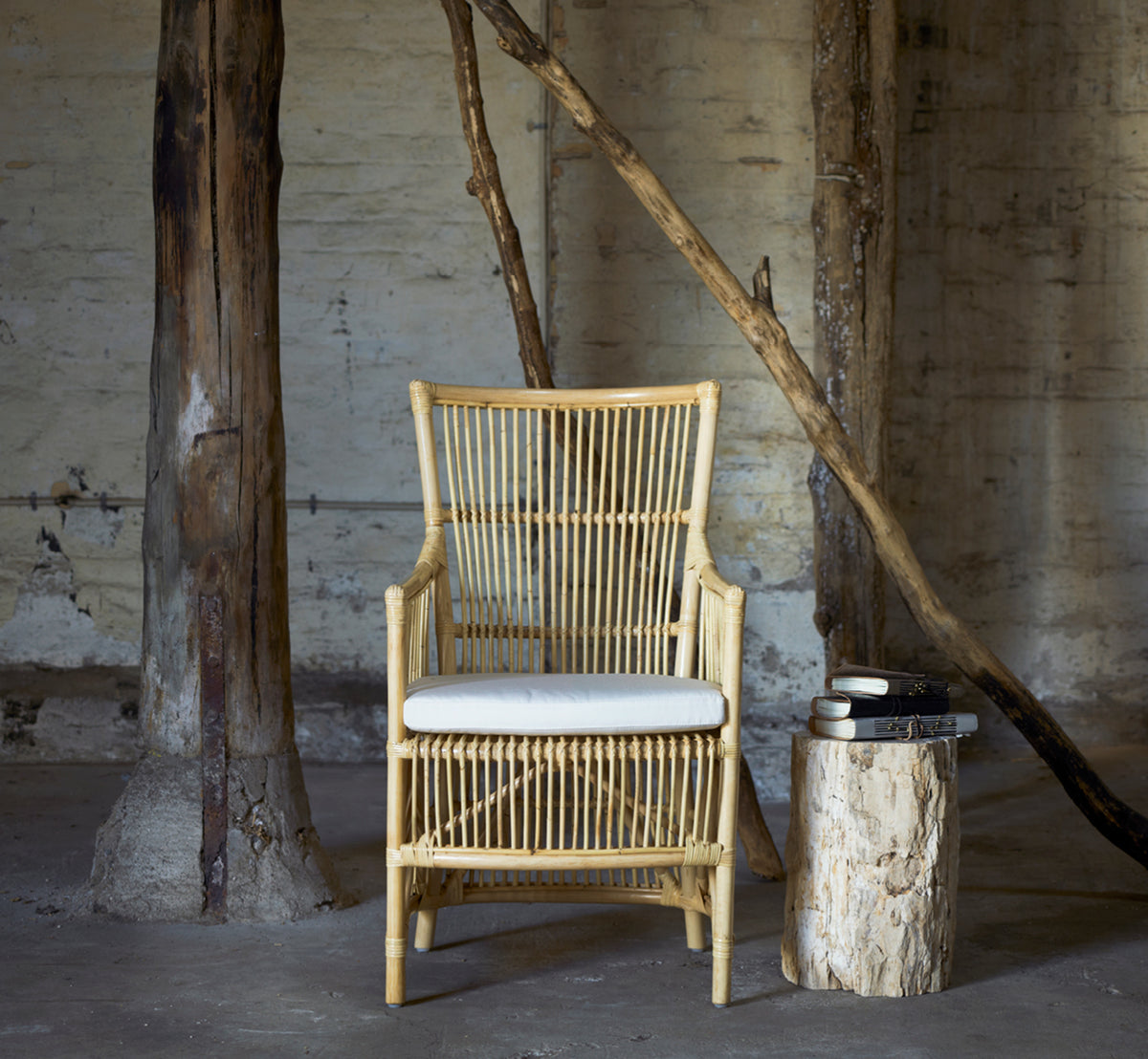 This is a lifestyle image of Davinci Dining Chair in natural rattan, in a bright interior with white panelled walls and herringbone parquet.