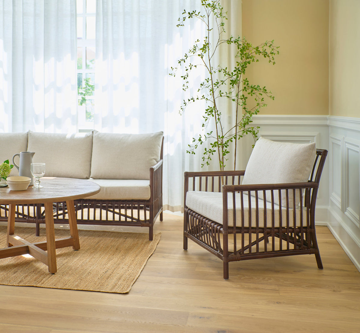 This is a lifestyle image of Caroline Lounge Chair in brown rattan. With sofa and teak coffee table in a bright living room.