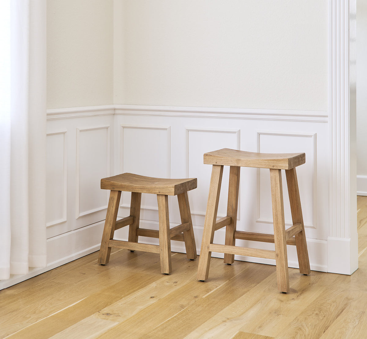 This is a lifestyle image of Charles Stool in teak indoor, in a bright white interior with wainscoting and herringbone parquet.