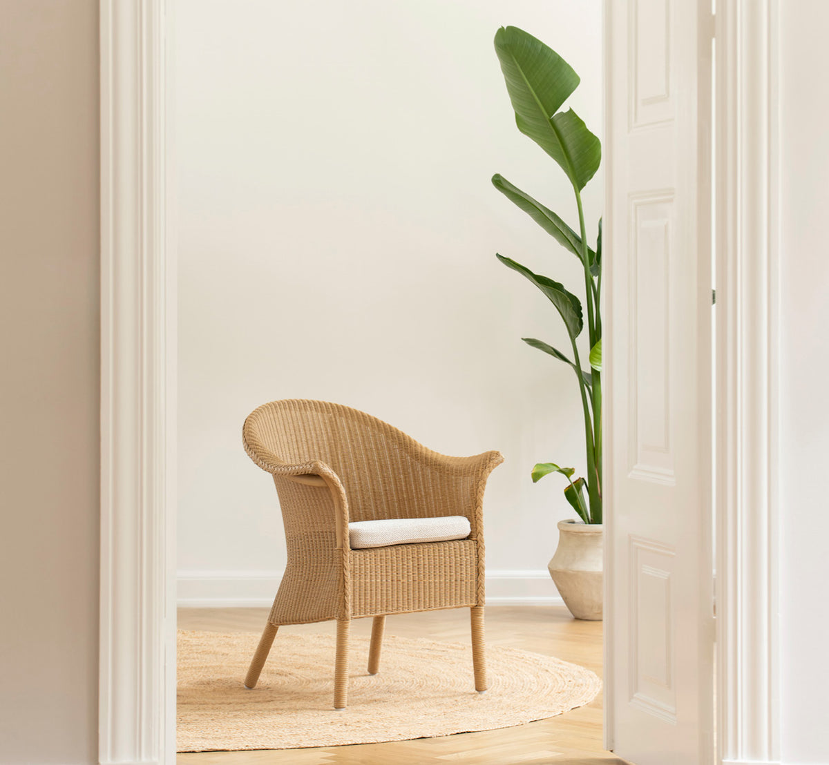 This is a lifestyle image of Classic Dining Chair in natural Loom Rattan Frame, in a bright interior with white panelled walls and herringbone.