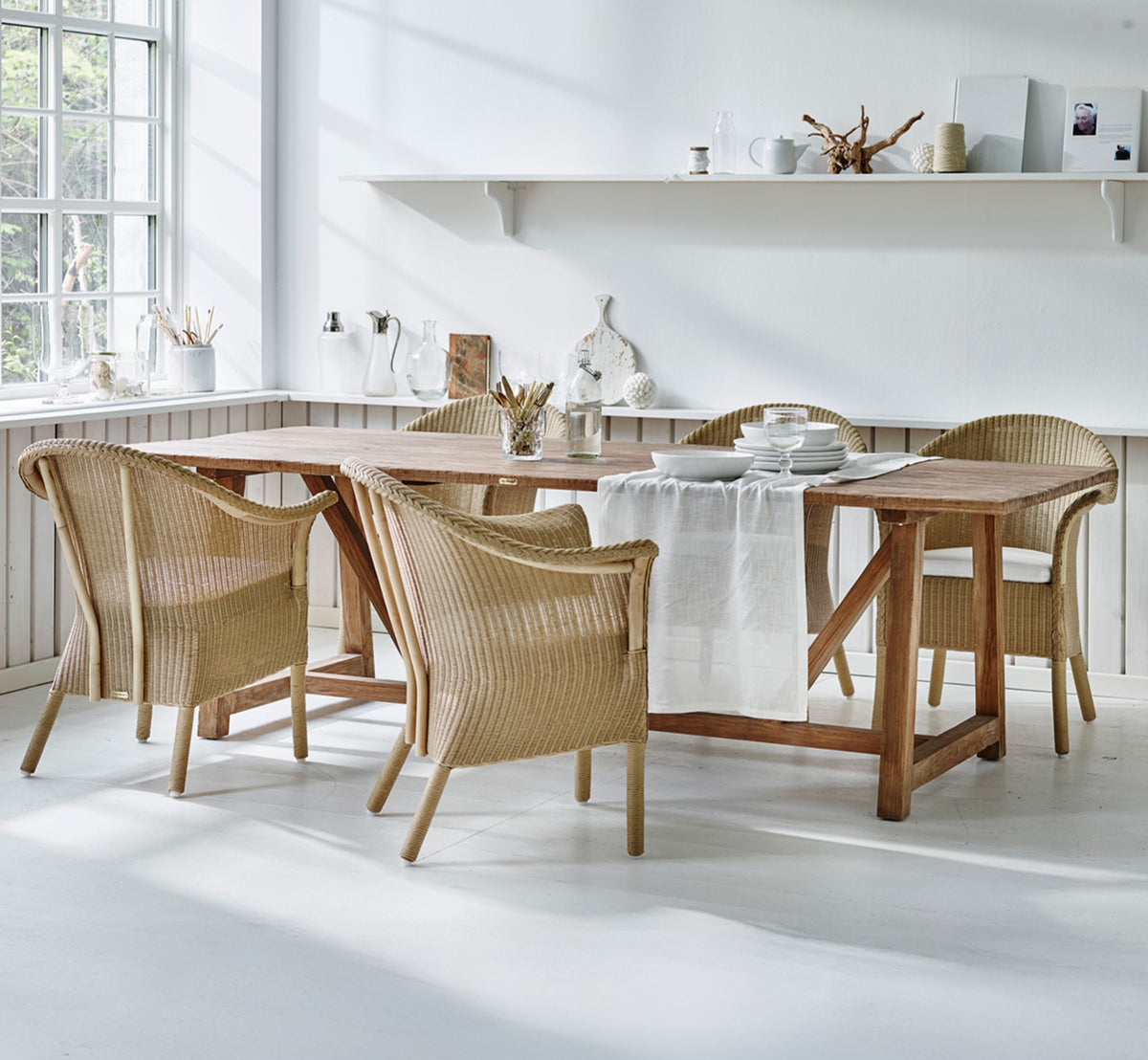 This is a lifestyle image of Classic Dining Chair in natural Loom Rattan Frame, in a bright interior with white panelled walls and herringbone.