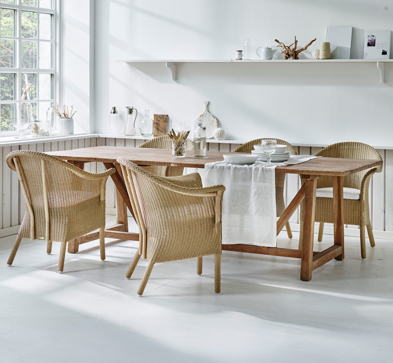 This is a lifestyle image of Classic Dining Chair in natural Loom Rattan Frame, in a bright interior with white panelled walls and herringbone.