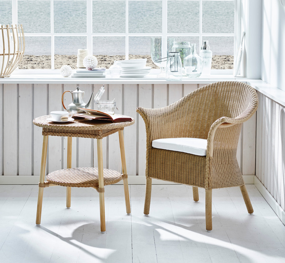This is a lifestyle image of Classic Dining Chair in natural Loom Rattan Frame, in a bright interior with white panelled walls and herringbone.