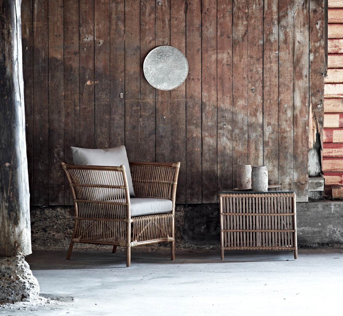 This is a lifestyle image of Donatello Lounge Chair in antique rattan, in a bright living room with herringbone parquet and lush greenery.