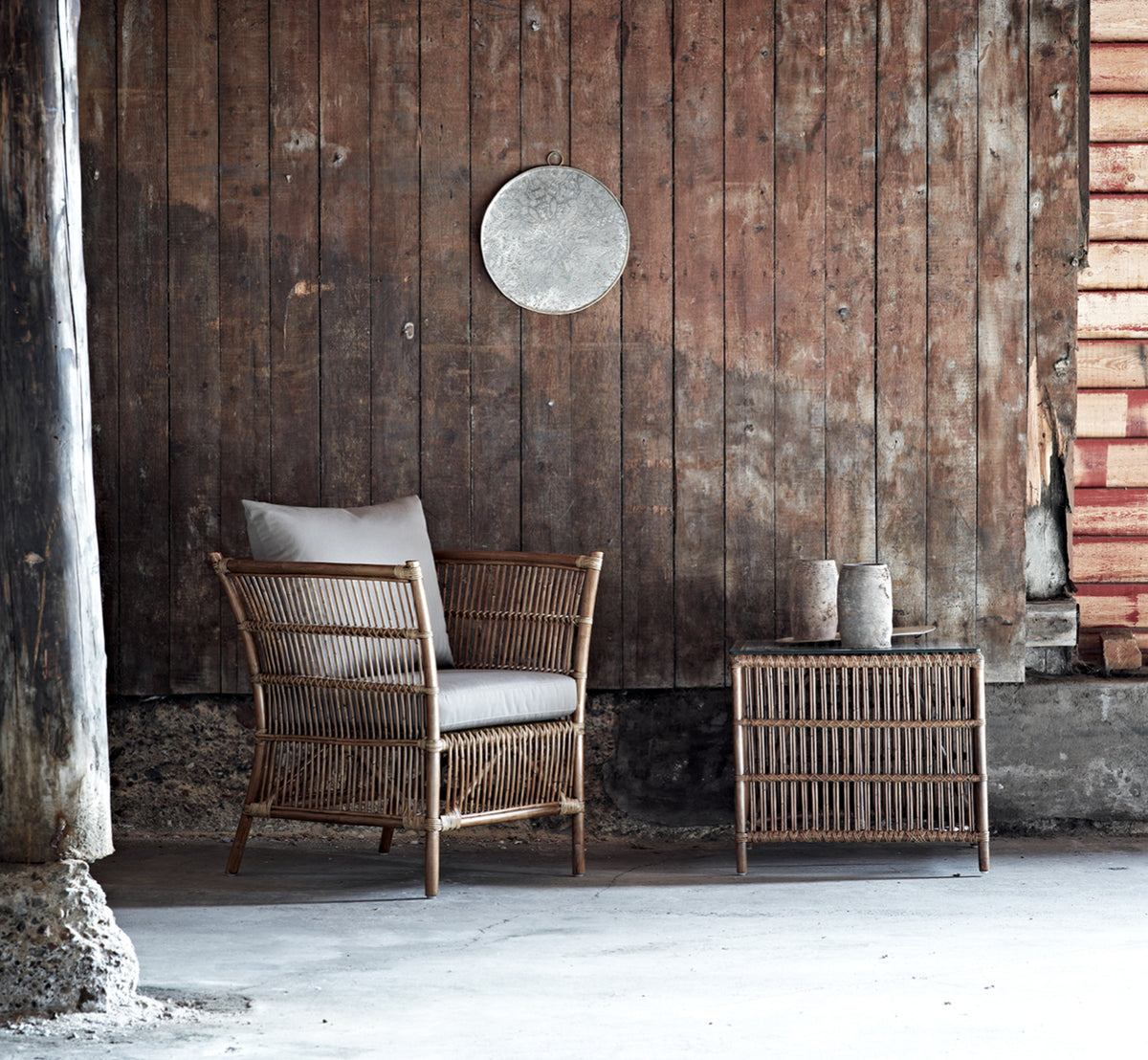 This is a lifestyle image of Donatello Side Table in antique rattan, in a bright interior with white panelled walls and herringbone parquet.