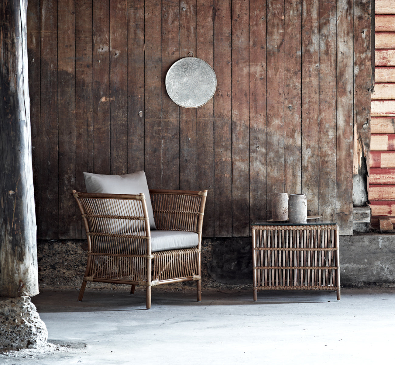 This is a lifestyle image of Donatello Side Table in antique rattan, in a bright interior with white panelled walls and herringbone parquet.