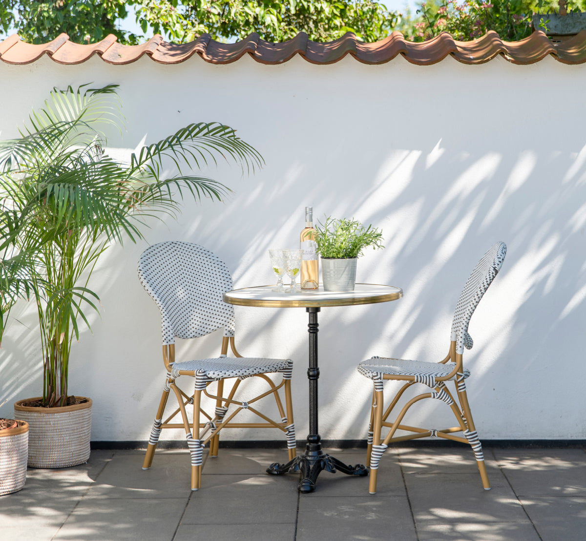 This is a lifestyle image of Isabell in almond aluminium frame White w cappuccino dot ArtFibre, in a lush garden patio with stone tile and a.