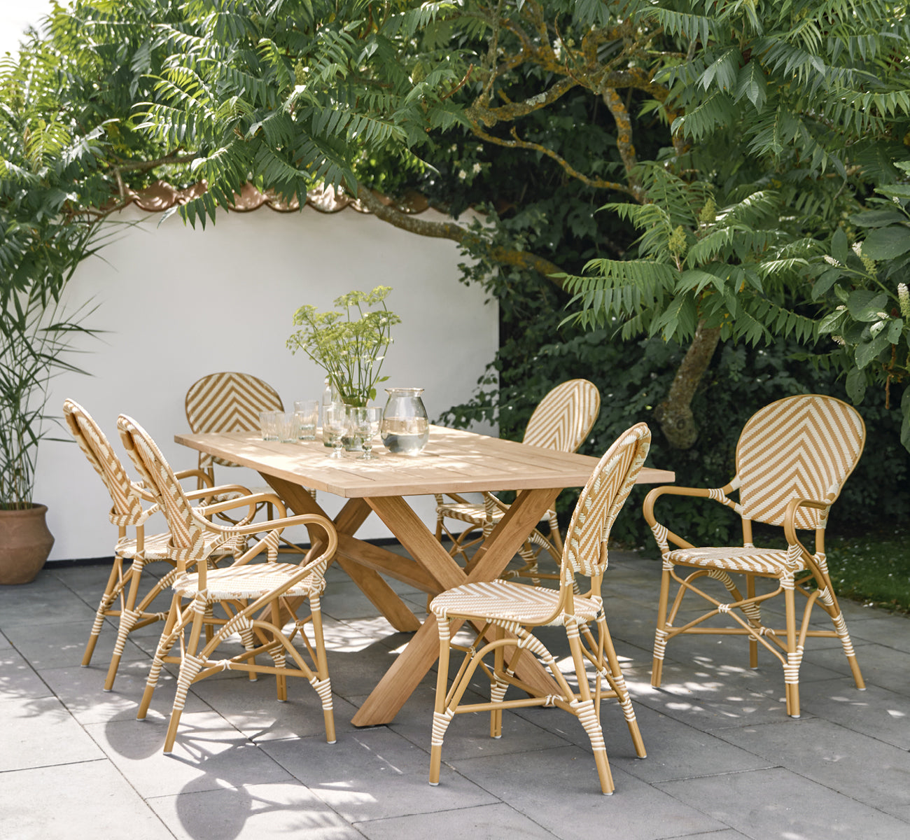 This is a lifestyle image of Isabell in almond aluminium frame Chevron Honey Ivory ArtFibre, in a lush garden patio with stone tile and a.