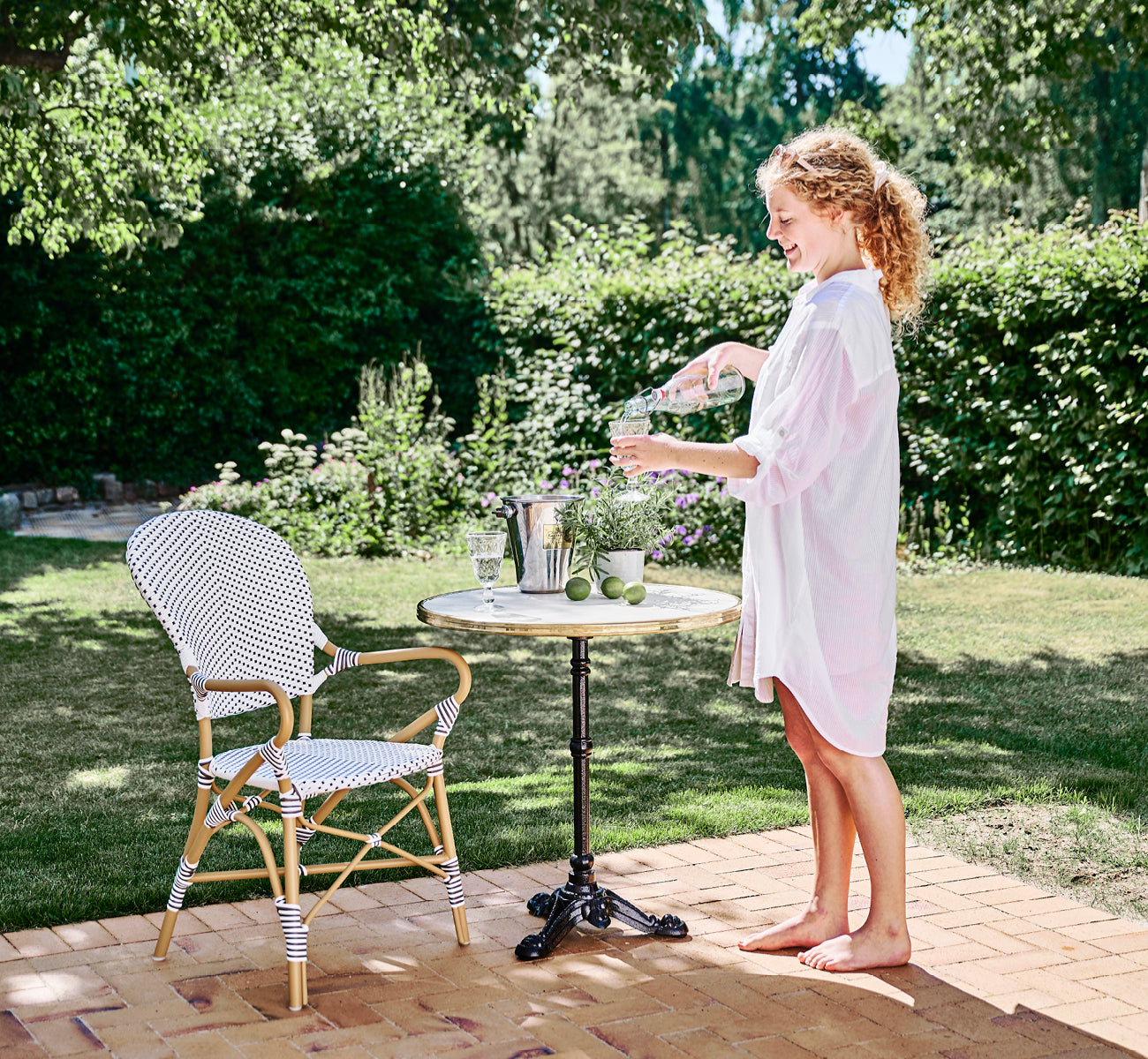 This is a lifestyle image of Isabell in almond aluminium frame White w cappuccino dot ArtFibre, in a lush garden patio with stone tile and a.