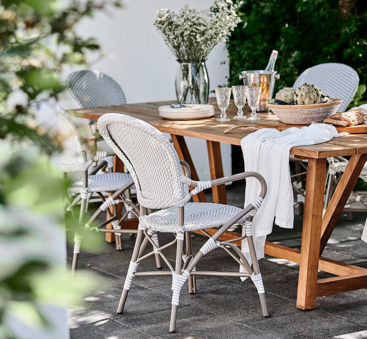 This is a lifestyle image of Isabell in taupe aluminium frame Grey w white dot ArtFibre, in a lush garden patio with stone tile and a greenery-clad.