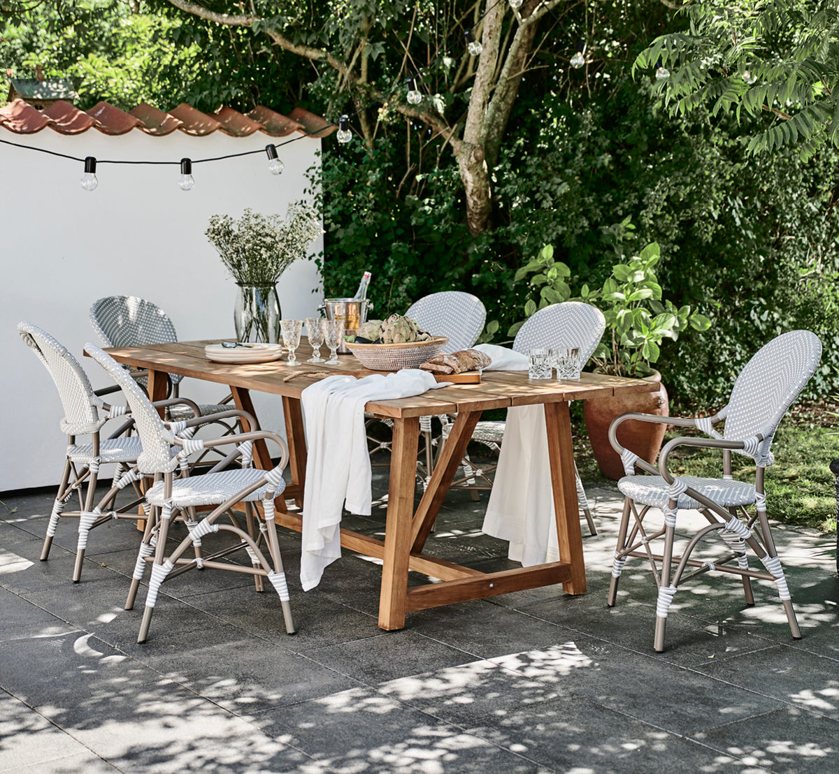 This is a lifestyle image of Isabell in taupe aluminium frame Grey w white dot ArtFibre, in a lush garden patio with stone tile and a greenery-clad.