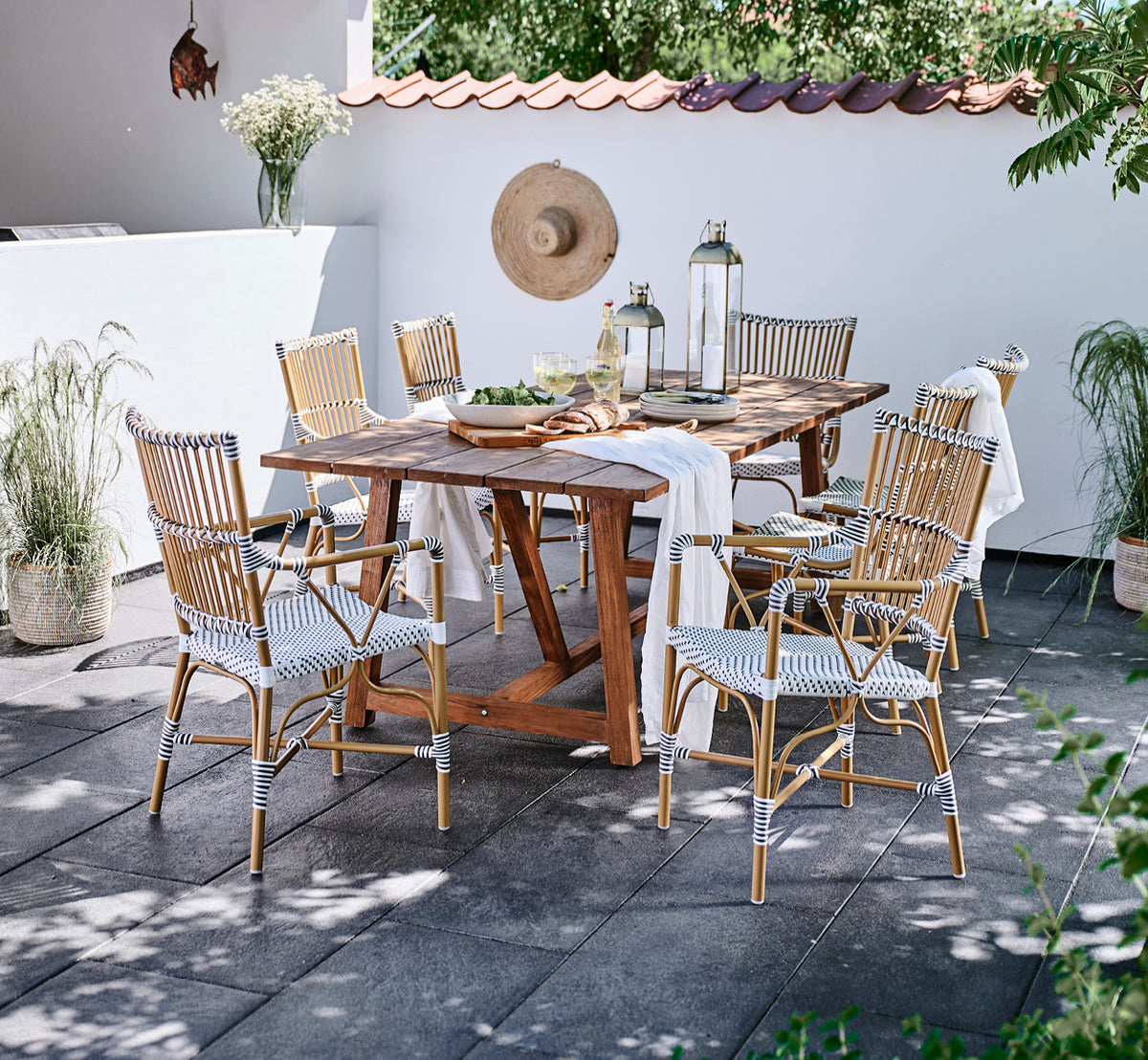 This is a lifestyle image of Monique Exterior Dining Armchair in white w cappuccino dot ArtFibre. Around a teak table on a terrace.