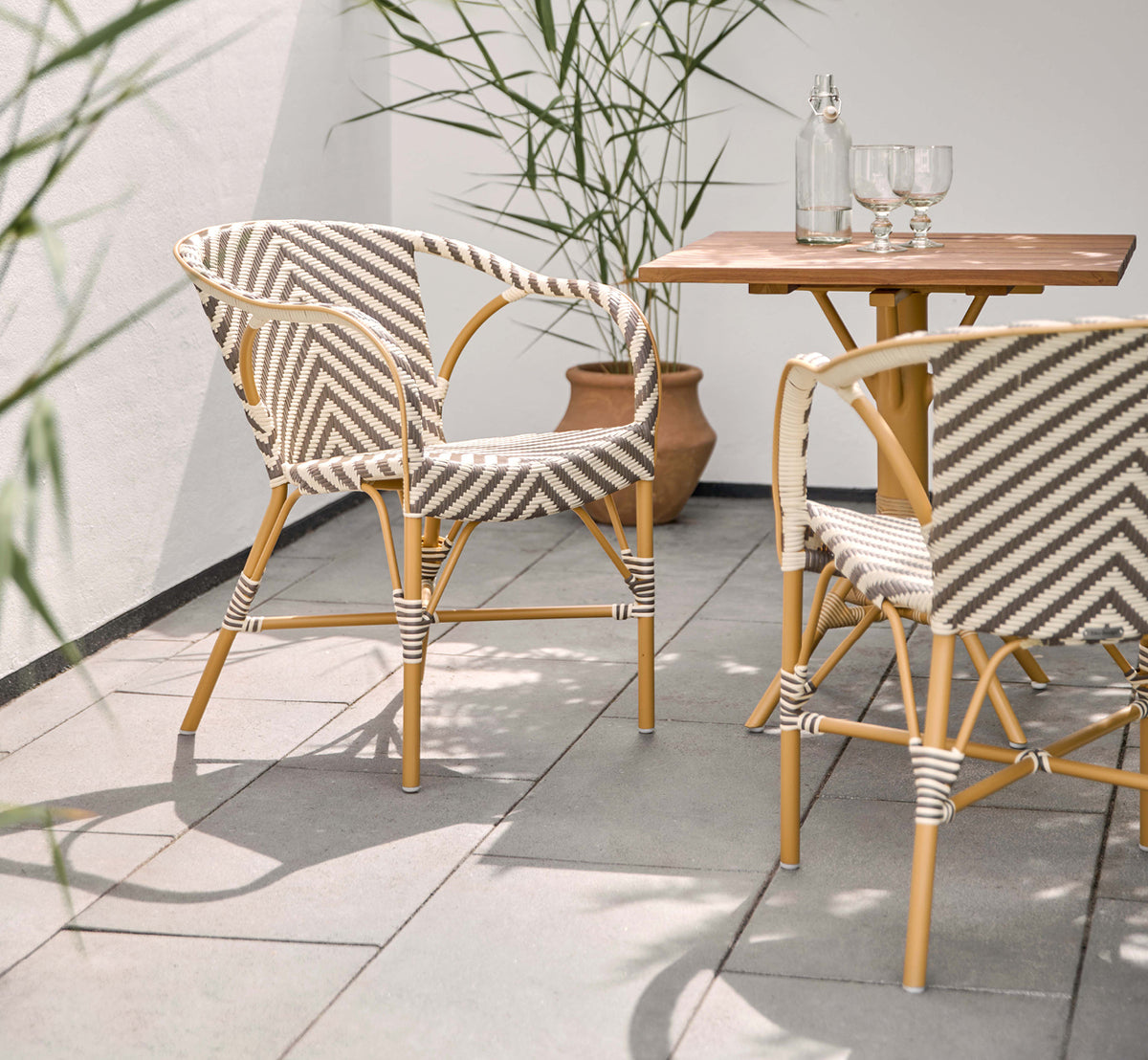 This is a lifestyle image of Madeleine Exterior Dining Chair in almond aluminum frame chevron cappuccino ivory ArtFibre. Sunny terrace with table.