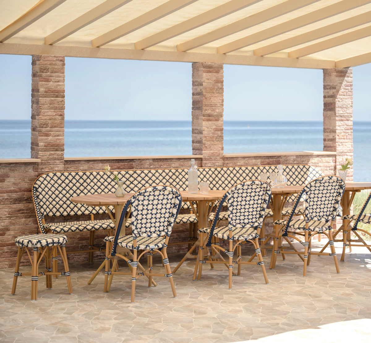 This is a lifestyle image of Sofie Exterior 6-Seater Bench in almond aluminium frame starweave ivory navy blue cappuccino artfibre. By the sea.