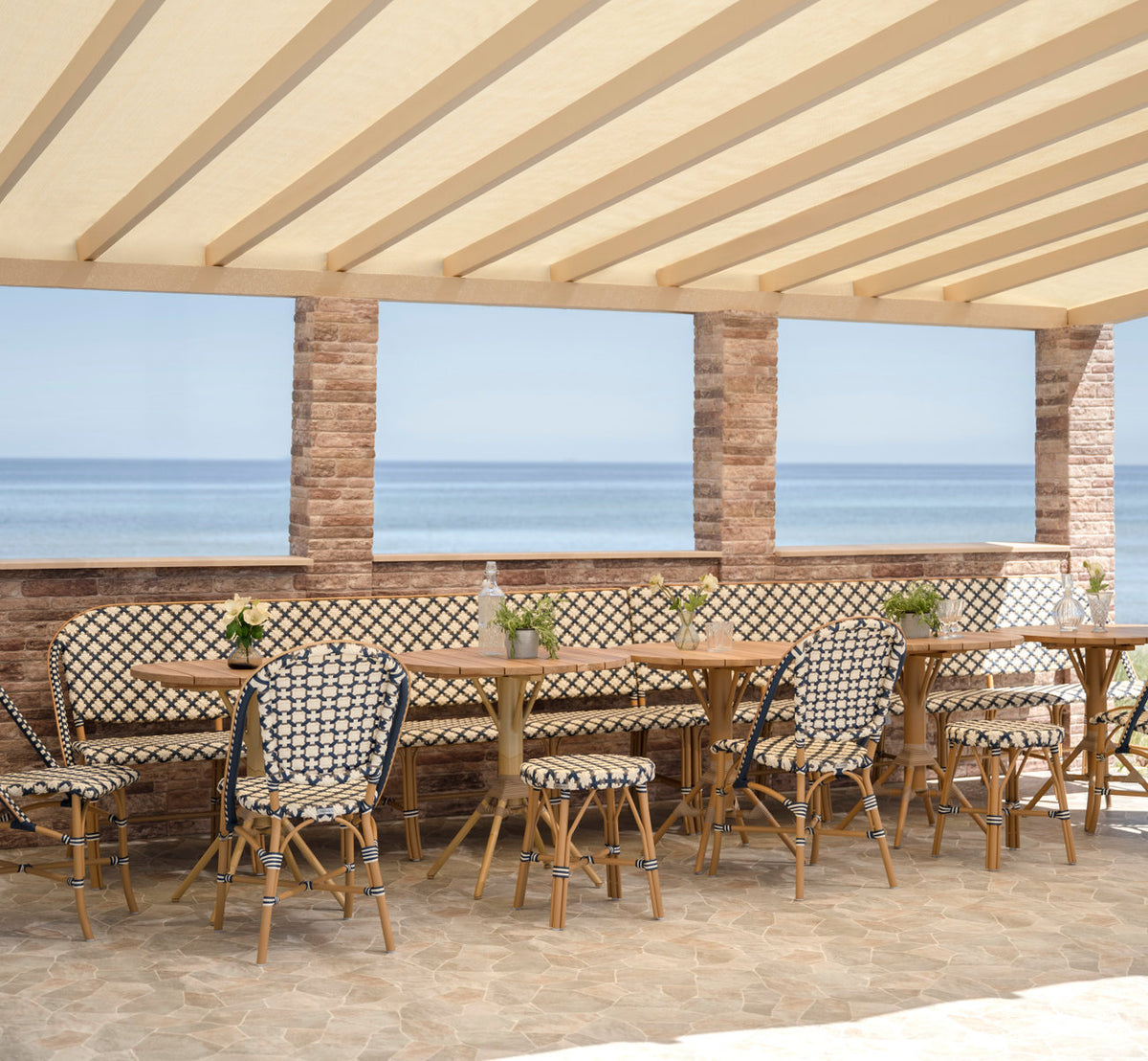This is a lifestyle image of Sofie Exterior 8-Seater Bench in almond aluminium frame starweave ivory navy blue cappuccino artfibre. By the sea.