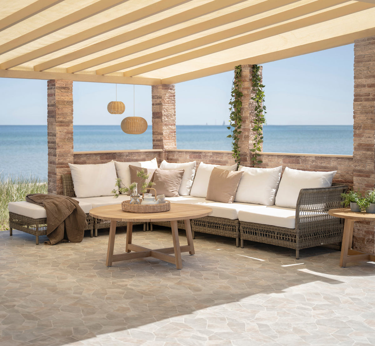 This is a lifestyle image of Mona Exterior Modular Sofa-Pouf Module in antique grey artfibre aluminium. Under a pergola by the sea.