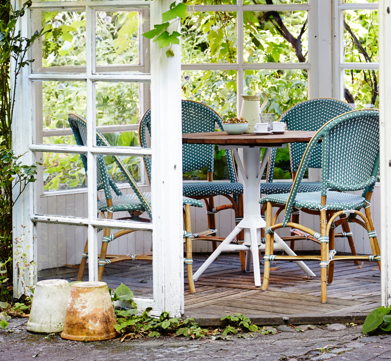 This is a lifestyle image of Sofie Dining Chair in salvie green w white dot artfibre skin on natual rattan frame. Styled in a bright interior setting.