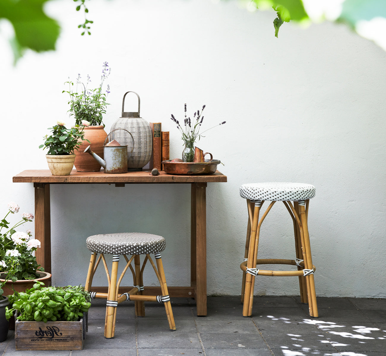 This is a lifestyle image of Simone Counter Stool in white w cappuccino dot ArtFibre Skin on Rattan frame. By a rustic potting table with plants.