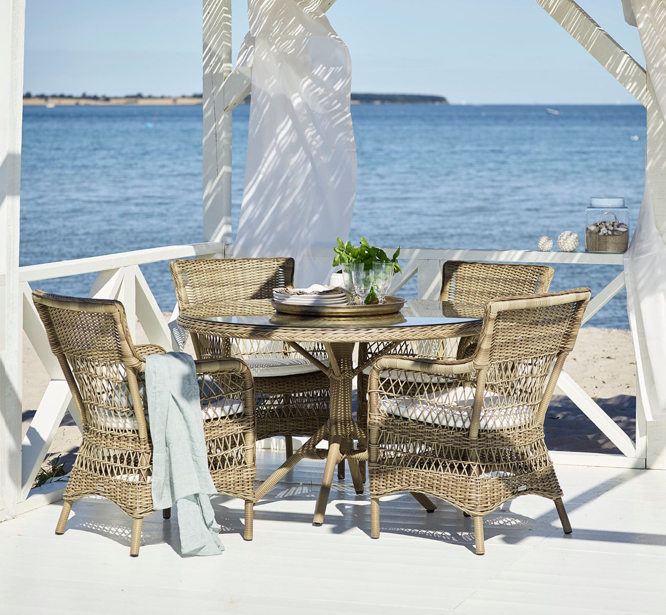 This is a lifestyle image of Marie Exterior Armchair in antique grey artfibre aluminium. On a covered seaside pavilion with ocean.