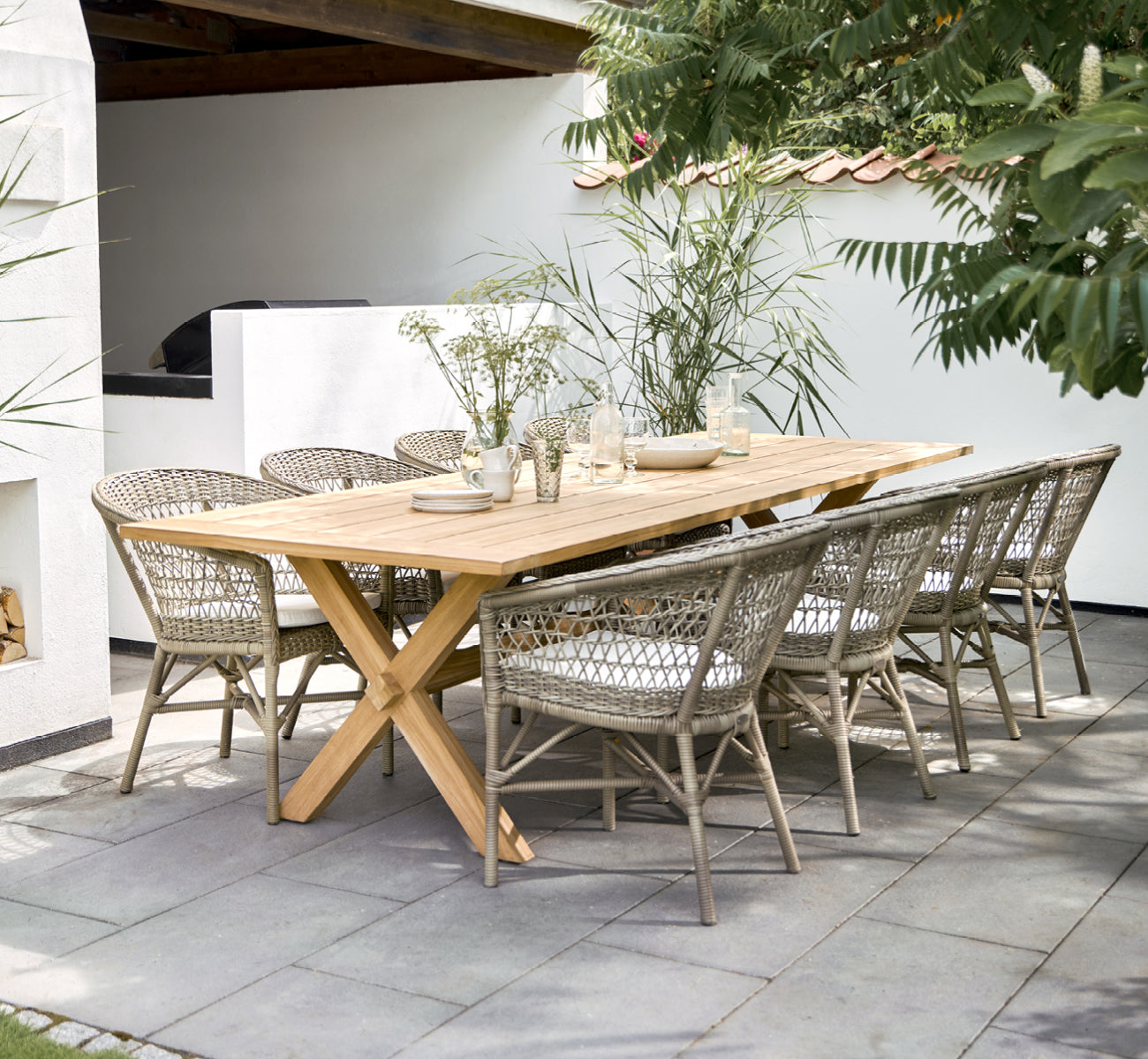 This is a lifestyle image of Emma Exterior Dining Chair in antique Grey ArtFibre Aluminium, on a bright coastal terrace with a reed roof shade and.