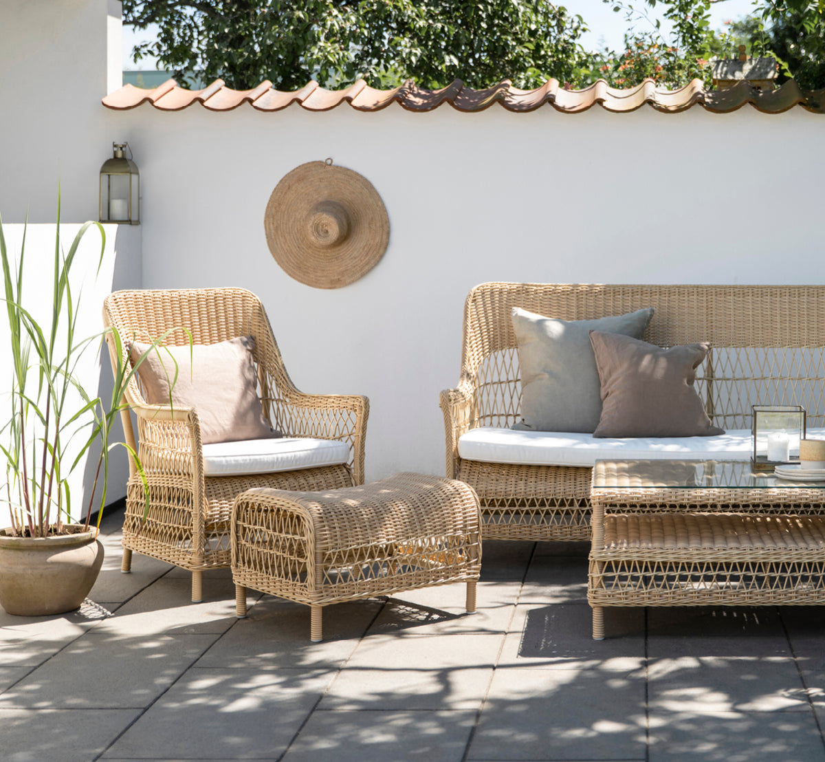 This is a lifestyle image of Dawn Lounge Chair in natural ArtFibre Aluminium, on a coastal terrace with sea views, beach grasses and white columns.