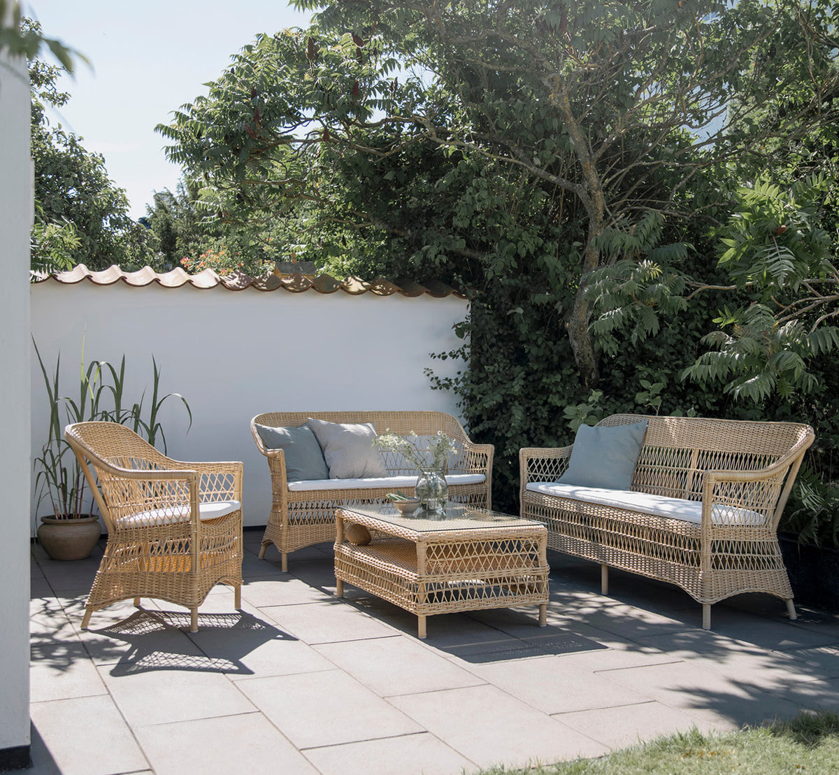 This is a lifestyle image of Charlot 3 Seater Sofa in natural ArtFibre Aluminium, on a coastal terrace with reed roof shade and sea views.