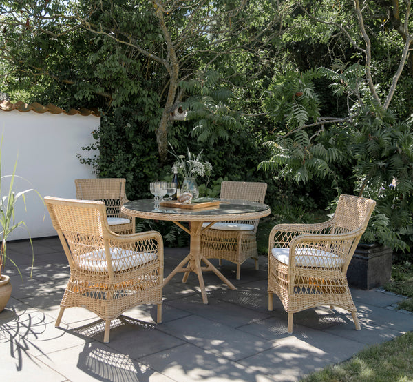 This is a lifestyle image of Grace Exterior Dining Table in natural ArtFibre Aluminium, in a lush garden patio with stone tile flooring and.
