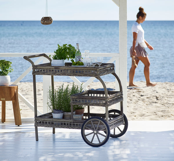 This is a lifestyle image of James Trolley in antique grey artfibre aluminium, on a beach terrace under a white pergola with sea views.