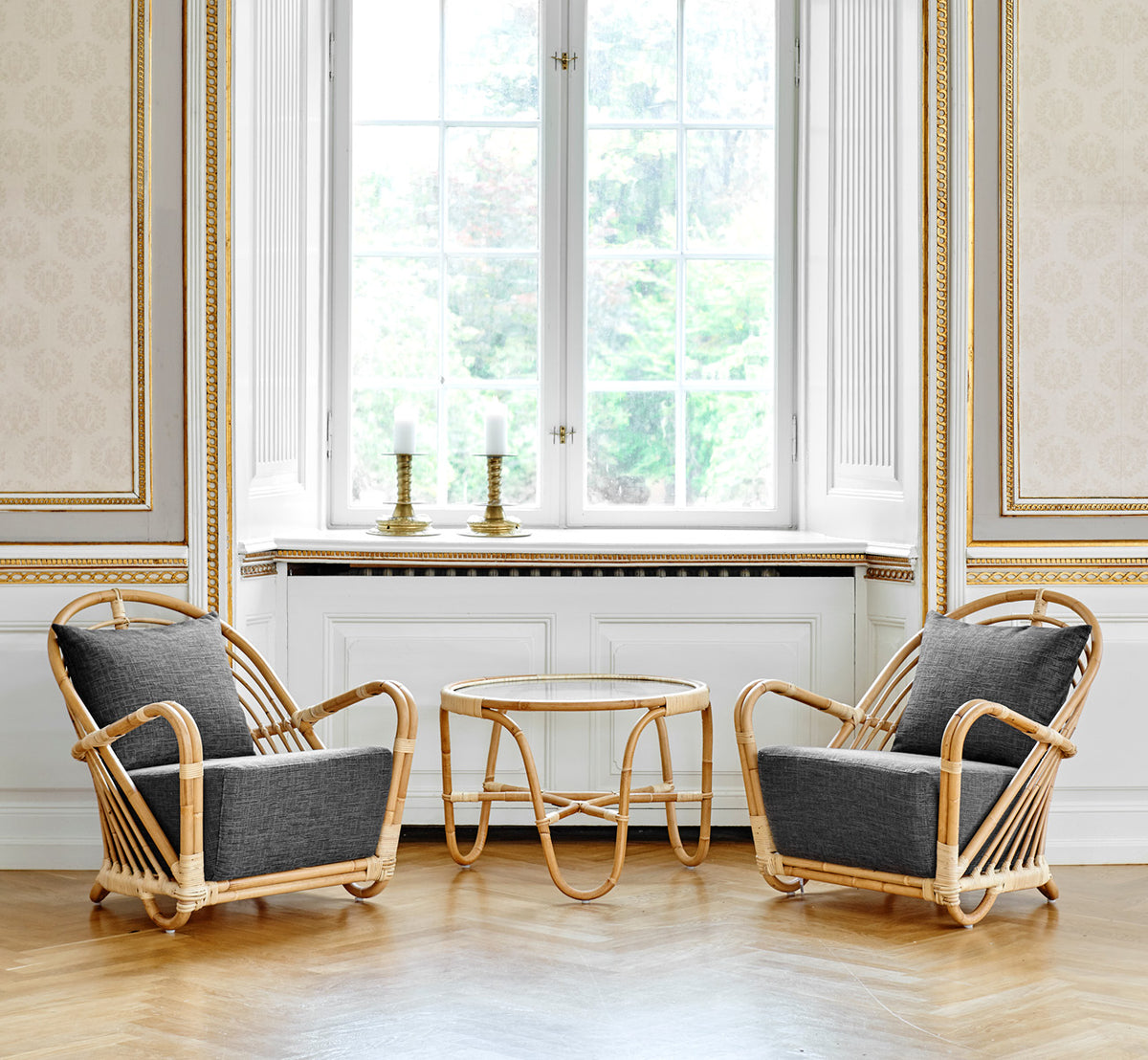 This is a lifestyle image of Charlottenborg Lounge Chair in polished Natural Rattan, in an elegant classical interior with ornate golden mouldings.