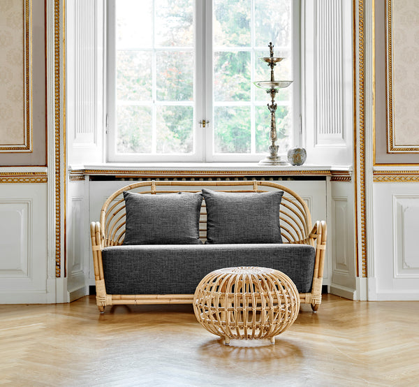 This is a lifestyle image of Charlottenborg Sofa in polished Natural Rattan, in an elegant classical interior with ornate golden mouldings.