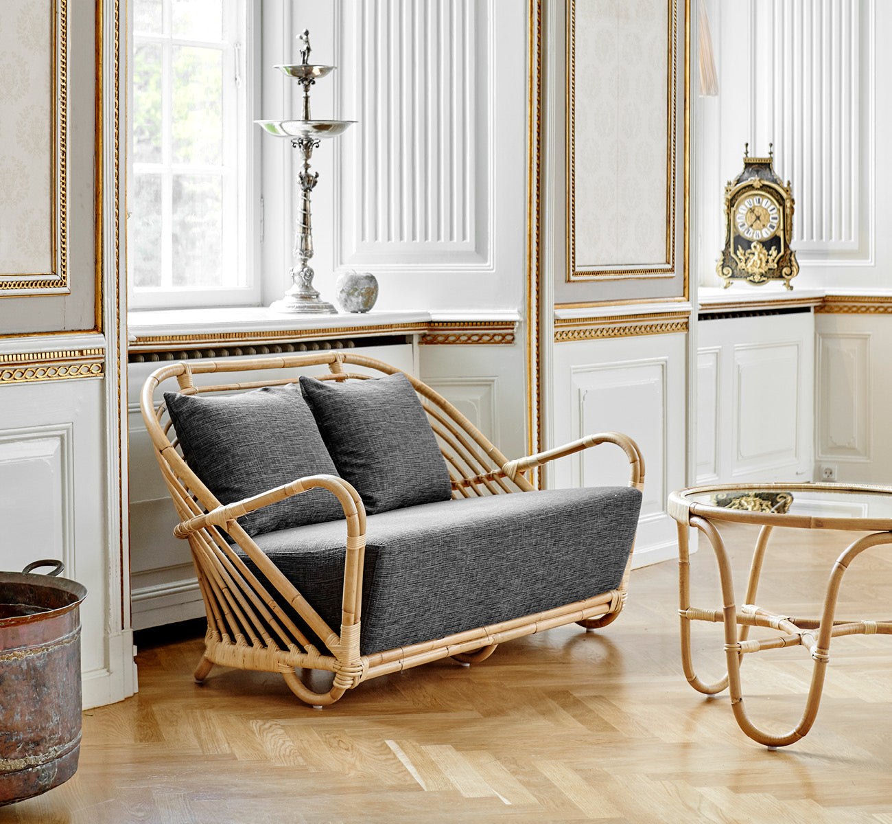 This is a lifestyle image of Charlottenborg Sofa in polished Natural Rattan, in an elegant classical interior with ornate golden mouldings.
