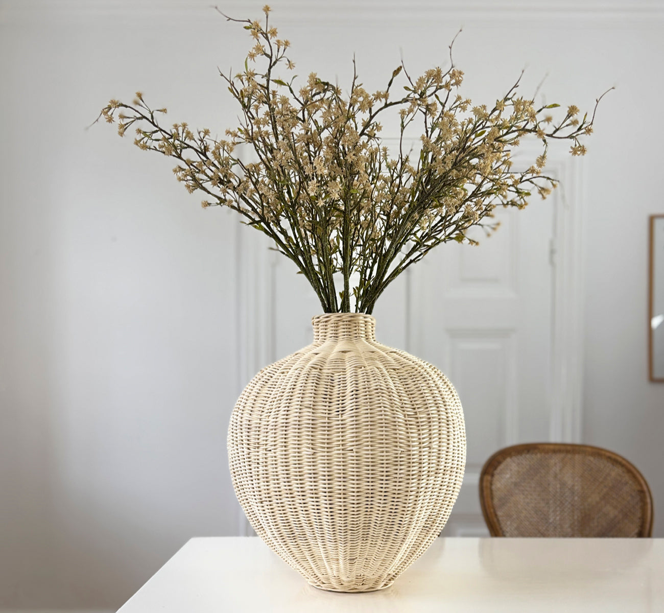This is a lifestyle image of Flumen Basket in natural core weave iron frame, in a bright white interior with wainscoting, styled with dried flowers.