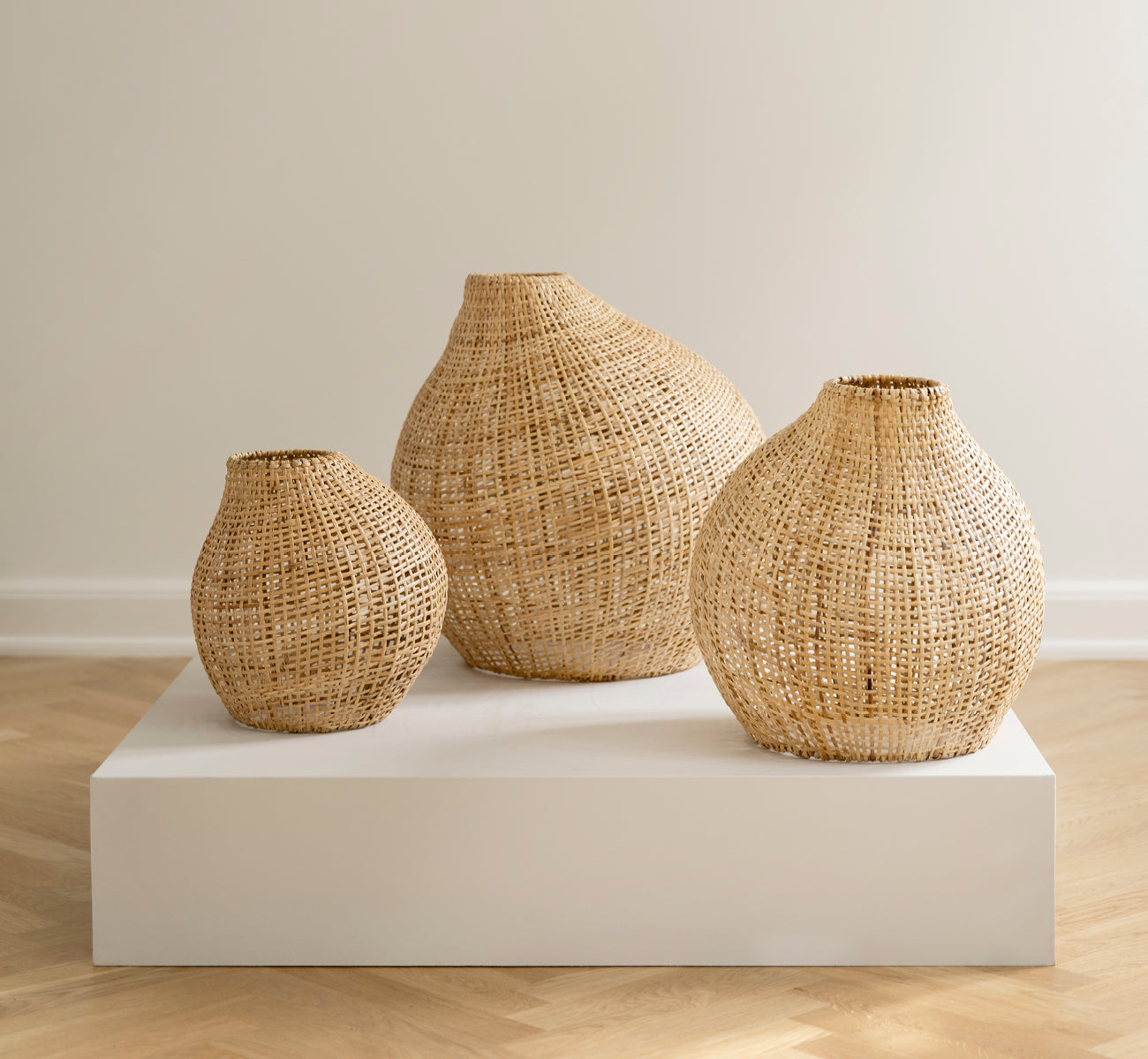This is a lifestyle image of Figura Floor Lampshade in light natural weave rattan, displayed on a white platform against a neutral interior backdrop.