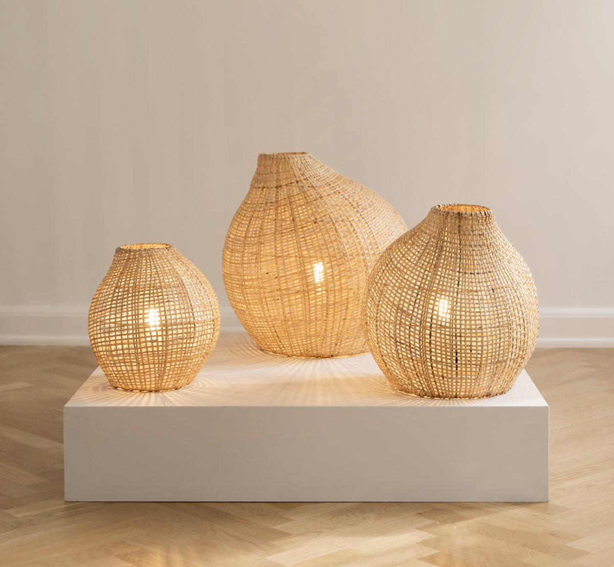 This is a lifestyle image of Figura Floor Lampshade in light natural weave rattan, displayed on a white platform against a neutral interior backdrop.