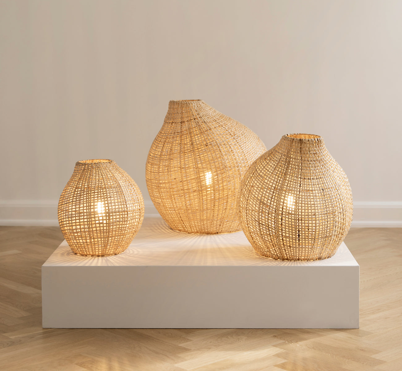 This is a lifestyle image of Figura Floor Lampshade in light natural weave rattan, displayed on a white platform against a neutral interior backdrop.