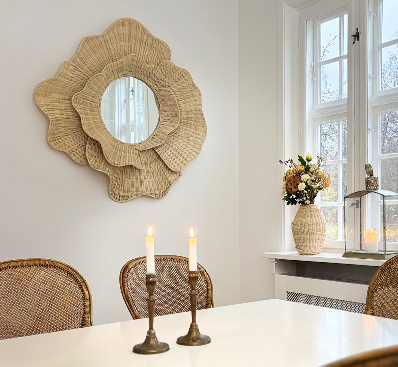 This is a lifestyle image of Floral Mirror in natural core weave iron frame, hung in a bright dining room with candlesticks and natural window light.