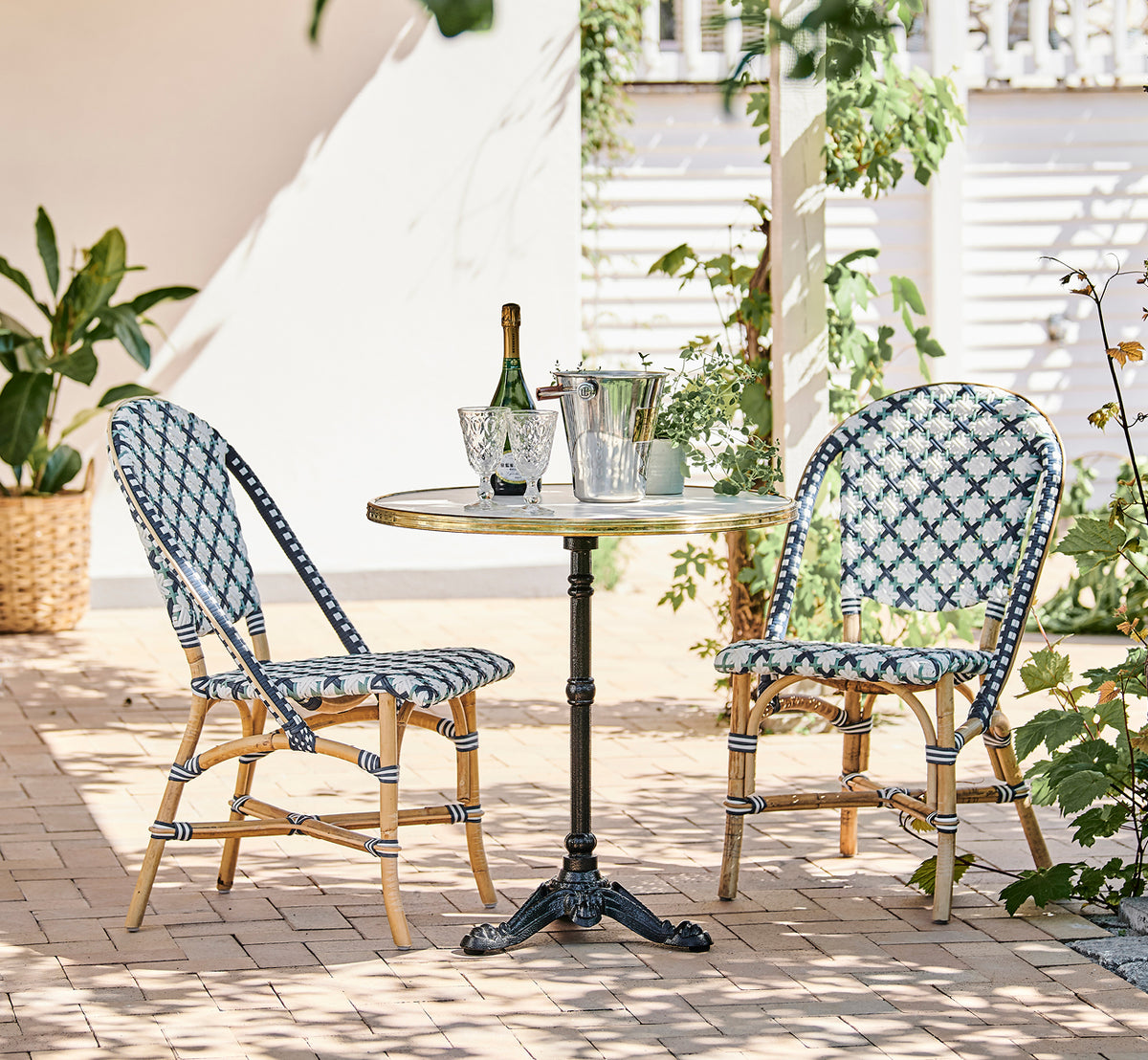This is a lifestyle image of Lyon Café Table Versalite Marble Ø70 cm in cast iron. Sunny terrace with bistro chairs and a champagne bottle.