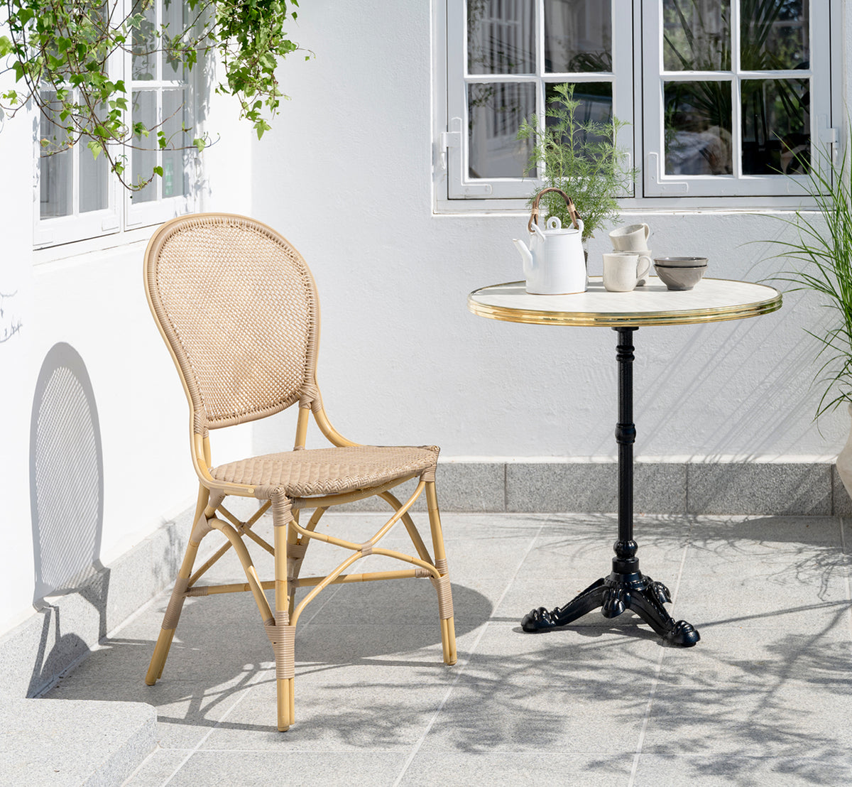 This is a lifestyle image of Lyon Café Table Versalite Marble Ø70 cm in cast iron. Courtyard with a dining chair and coffee set on the table.