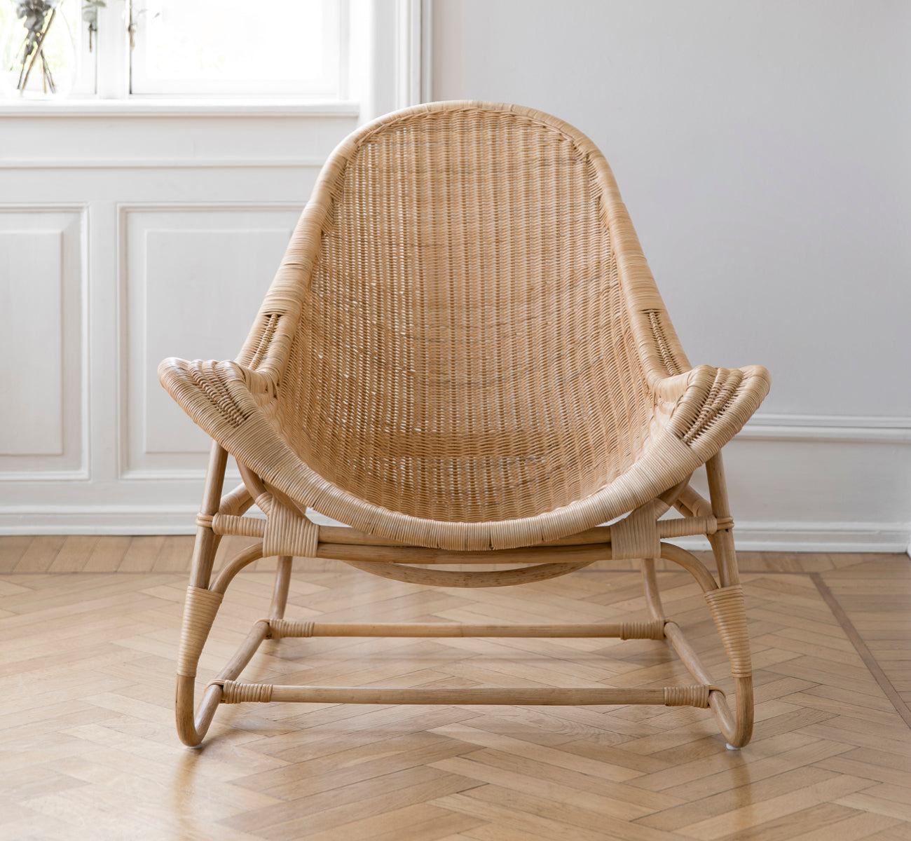 This is a lifestyle image of Pacifique Lounge Chair in natural core weave rattan frame. Styled in a bright interior setting.