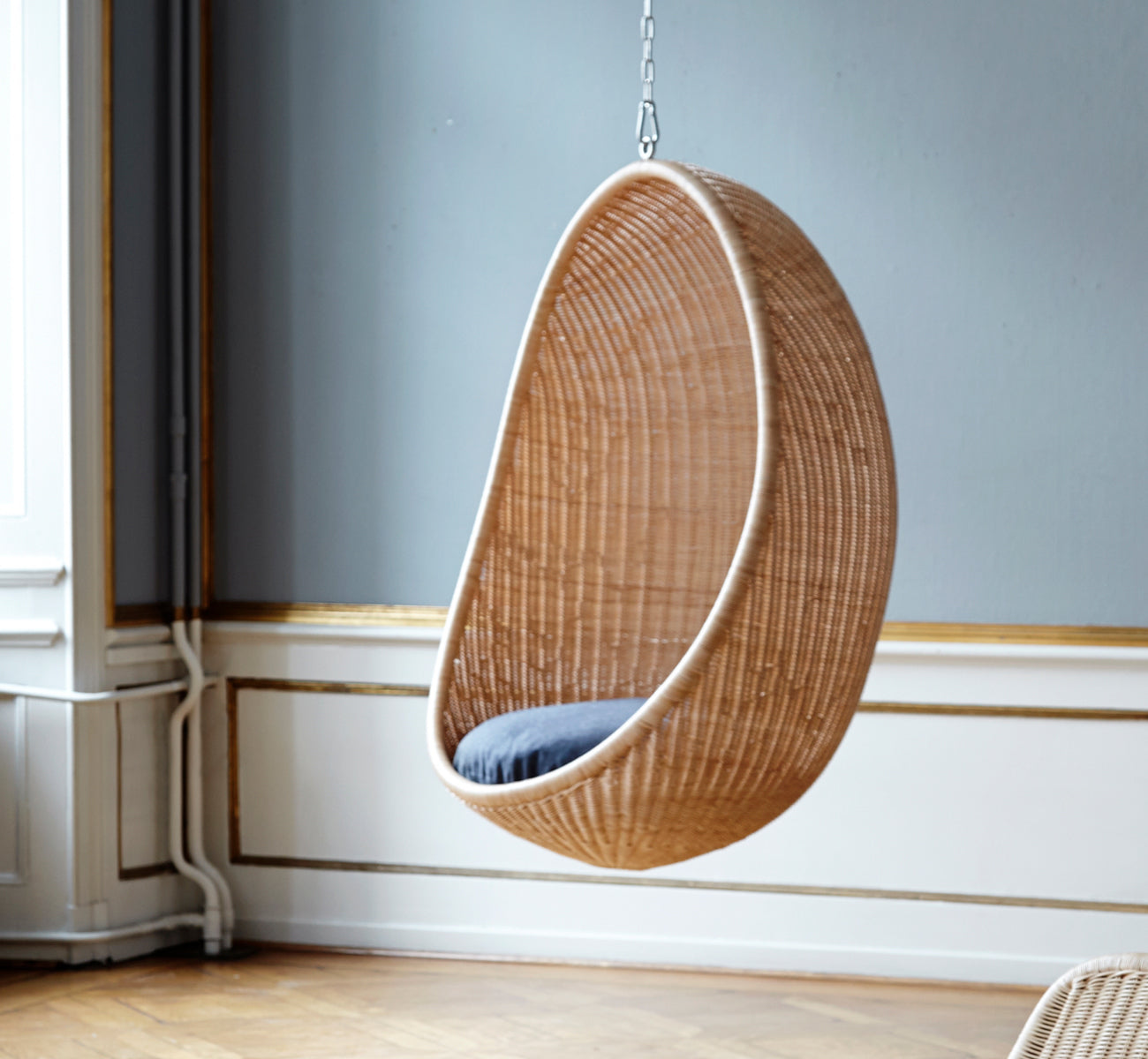 This is a lifestyle image of Hanging Egg Chair in natural core weave Rattan frame, in an elegant classical interior with ornate golden mouldings.