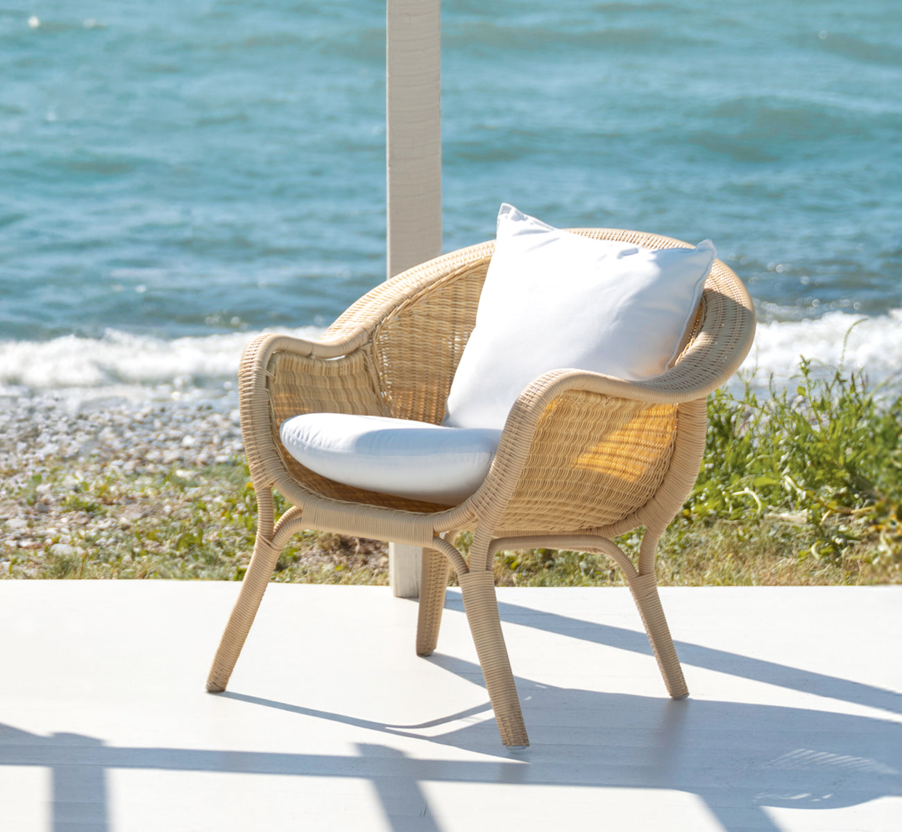 This is a lifestyle image of Madame Lounge Chair in natural core weave ArtFibre Aluminium, on an open coastal terrace at sunset with sea views and.