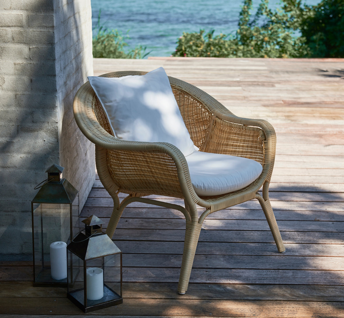 This is a lifestyle image of Madame Lounge Chair in natural core weave ArtFibre Aluminium, on an open coastal terrace at sunset with sea views and.